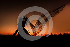 Silhouette of bride and groom kissing at sunset. The veil is flying