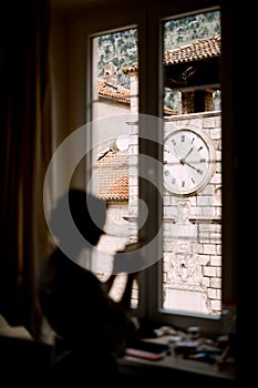 Silhouette of the bride standing by the window in a hotel room before the wedding ceremony. Clock tower in the window