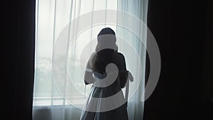 silhouette of a bride in a white long dress on the background of a bright window