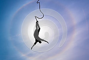 Silhouette of bungee jumper over blue sky background