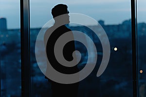 Silhouette of a Business Man looking out of high rise office window at night. a man in a classic suit near a window