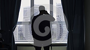 Silhouette of a business man talking on a mobile phone on the background of a window and city. Media. Successful