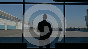 Silhouette of a businessman back overlooking the parking space behind the window. HDR. Rear view of a young man standing