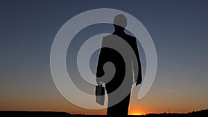 Silhouette of businessman with briefcase walking at sunset, against a blue sky