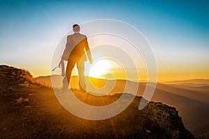 Silhouette of businessman in business suit on the top of the mountains at sunset