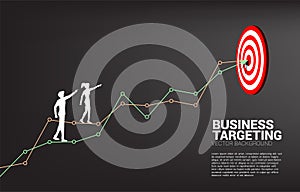 Silhouette of businessman and businesswoman point to dartboard on line graph to center of dartboard.