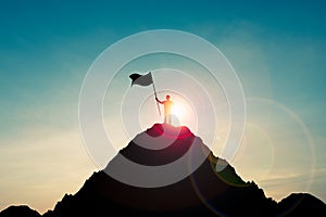 Silhouette of businessman holding flag on the top of mountain with over blue sky and sunlight. It is symbol of leadership