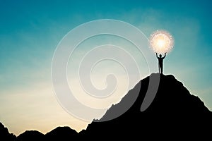 Silhouette of businessman holding world and connection line on the top of mountain with over blue sky and sunlight. It is symbol