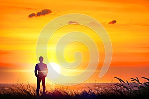 Silhouette of businessman standing on hill of sunset.