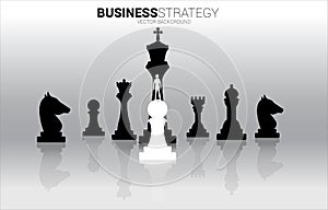 Silhouette of businessman standing on white pawn chess piece in front of all of black chess piece .