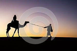 Silhouette of a camel and a cameleer at sunrise.