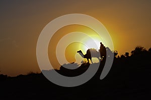 Silhouette of a camel cart and camel carrying tourists in Sam sand dunes, Jaisalmer. Located in the midst of the Thar Desert,