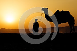 Silhouette of the Camel Trader crossing the sand dune during sun