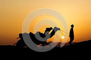 Silhouette of the Camel Trader crossing the sand dune .