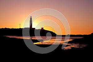 Silhouette of the Cape Trafalgar lighthouse surrounded by the ocean during the sunset in Spain