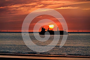 Silhouette of a cargo ship sailing on the ocean with the sunset behind. North sea, Zeeland. The Netherlands