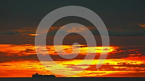 Silhouette cargo ship slow moving on horizon sea and sunset red yellow orange sky