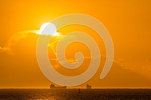 Silhouette of cargo ships on far distance at golden hour with solar disc