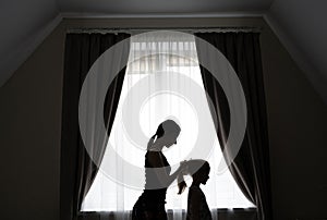 The silhouette of a caring mother combing her daughter`s hair