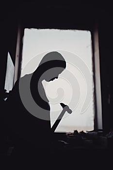 Silhouette of a carpenter working with a hammer against a window in a carpentry