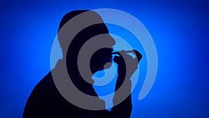Silhouette of cheerful senior man using birthday whistle on blue background. Celebration concept