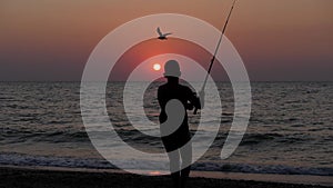 Silhouette of a child with a fishing rod against the background of a sea sunset. Sea fishing.