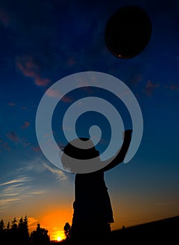 Silhouette of a child playing with ball at sunset