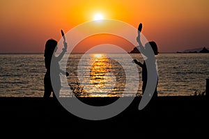 Silhouette of children playing tennis with sunset sun on a beach