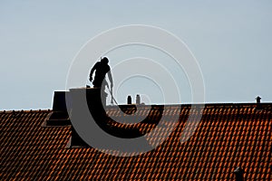 Silhouette of a chimney sweeper on top of a roof