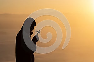 Silhouette of christian young man praying with a  cross at sunrise, Christian Religion concept background