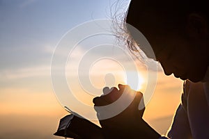Silhouette of christian young woman praying with a  cross and open the bible at sunrise, Christian Religion concept background photo