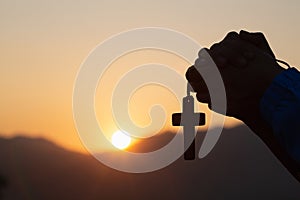 Silhouette of christian young woman praying with a cross at sunrise, Christian Religion concept background