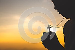 Silhouette of christian young woman praying with a  cross at sunrise, Christian Religion concept background