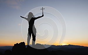 Silhouette of christian young woman praying with a  cross at sunrise, Christian Religion concept background