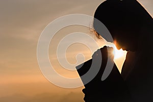Silhouette of christian young woman praying with  holy bible at sunrise, Christian Religion concept background