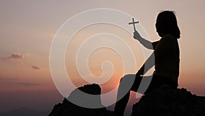 Silhouette of christianity woman catholic hand holding cross or crucifix pray to god at sunrise, person prayer in church concept