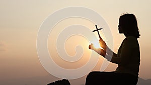 Silhouette of christianity woman catholic hand holding cross or crucifix pray to god at sunrise, person prayer in church concept