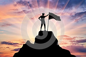 Silhouette of a climber with a flag on the top of the mountain which he subdued