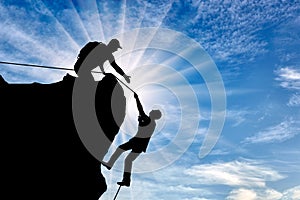 Silhouette of a climber who helps to climb the top of a man, throws him a rope and holds out his hand