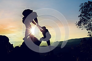 Silhouette climbing buddies help each other climb up the mountain at sunrise