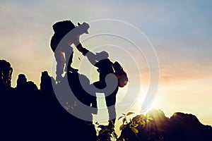 Silhouette climbing buddies help each other climb up the mountain at sunrise as the right lifestyle idea