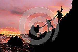 Silhouette of climbing team helping each by hand pull while climb mountain rock cliff
