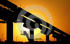 A silhouette of a construction site of monorail projects with crane, columns and tracks that is under construction at the sunset