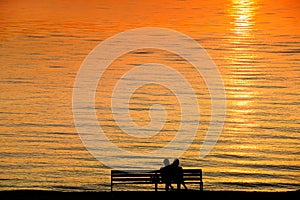 Silhouette of a couple on a bench at sunset against romantic ora