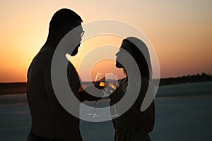 Silhouette of a couple with glasses on sunset background, man and woman clanging wine glasses with champagne at sunset dramatic sk