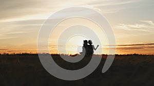 Silhouette of couple in golden field and beautiful sunset. Young and romantic family enjoying. Man hold woman in arms