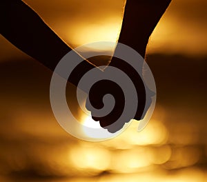 Silhouette of a couple holding hands on the beach. Closeup on hands of couple holding hands at sunset on the beach