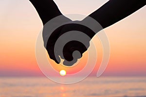 Silhouette of couple holding hands at sunset on the beach