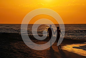 Silhouette of couple holding hands while walking on beach in a sunset