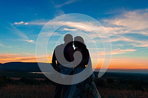 Silhouette of a couple hugging and kissing at sunset against the background of mountains and sea